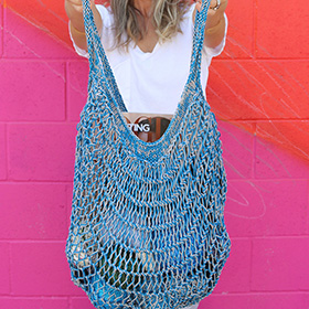 A model holding a blue knit farmer's tote