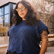 A model wearing a blue knit top with a black skirt and sunglasses