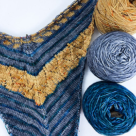 A work in progress knit shawl made of blue, gold, and grey yarn