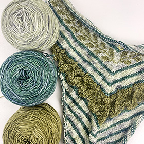 A work in progress knit shawl made of blue, green, and grey yarn