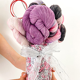 hands holding a vase of pink and black yarn arranged to look like a bouquet