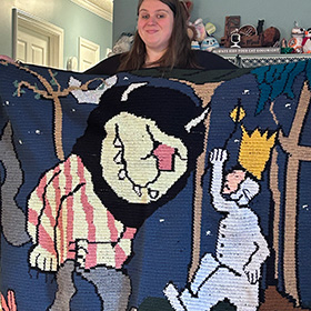 A model holding a blanket crocheted to look like Where The Wild Things Are