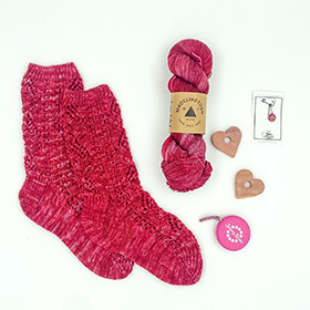 A pair of pink knit socks next to a skein of pink yarn and knitting accessories