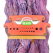 A skein of purple speckled yarn with a Friends inspired needle gauge