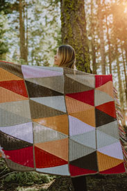 A model holding a triangle patterned blanket in the woods